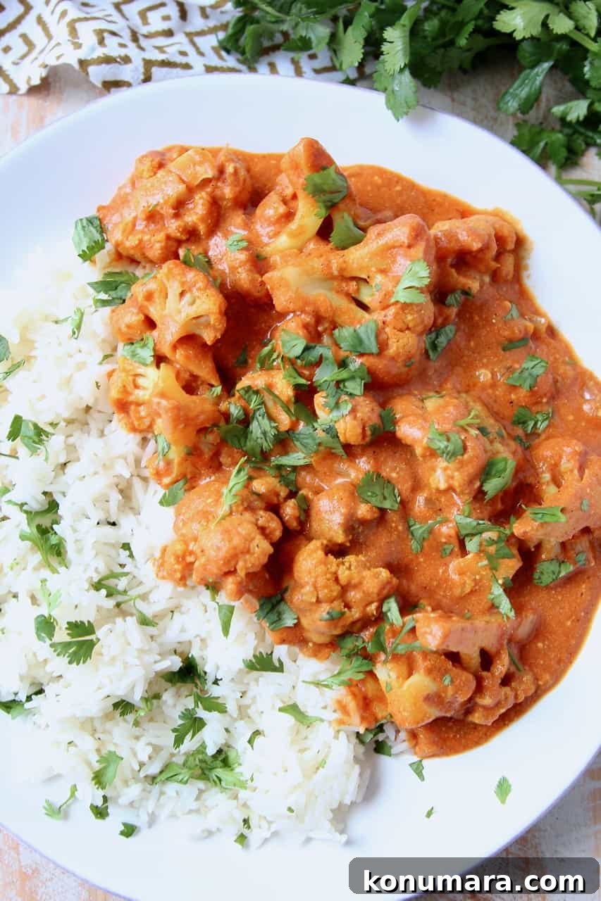 Creamy Indian Butter Cauliflower Curry Recipe 2 Cauliflower covered in curry sauce on plate with rice and cilantro