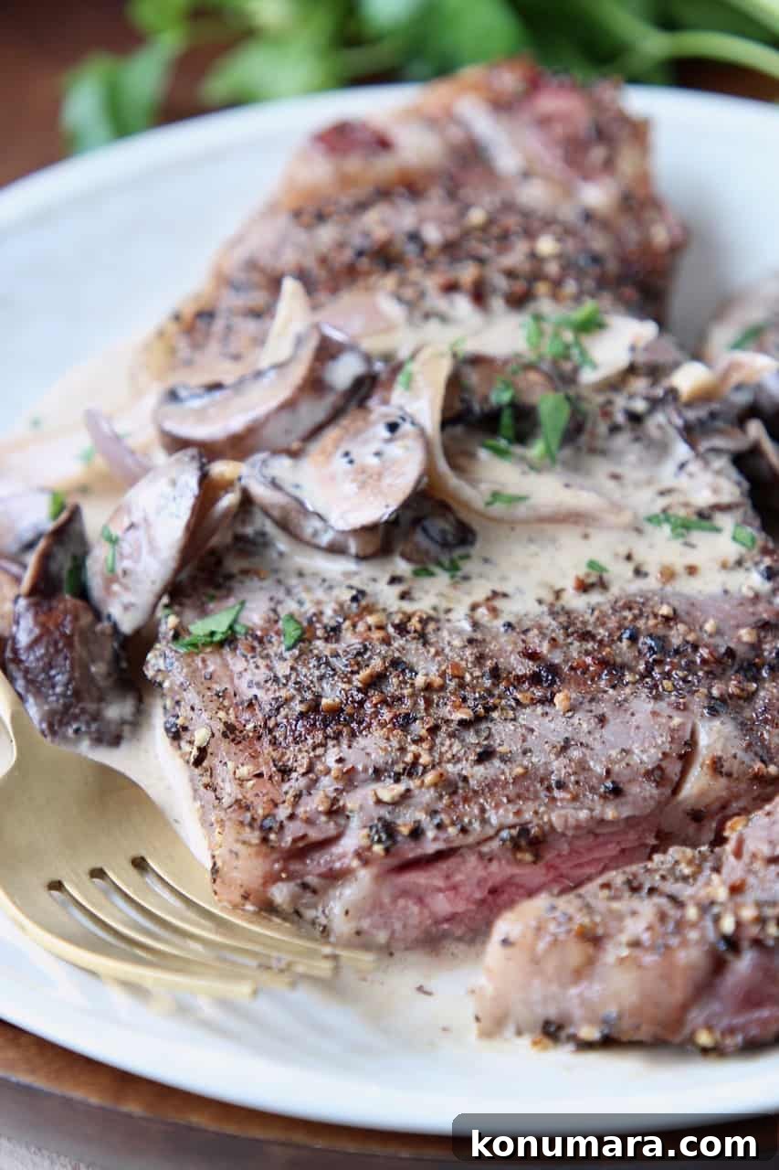 Grilled Peppercorn Crusted New York Strip with Mushroom Sauce 2 Sliced steak on plate with fork, covered in creamy mushroom sauce