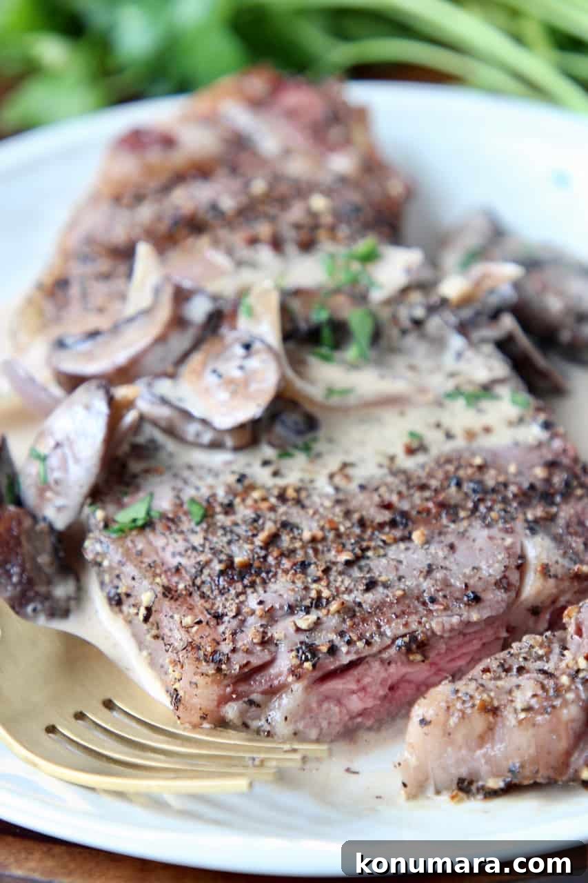 Grilled Peppercorn Crusted New York Strip with Mushroom Sauce 5 Sliced peppercorn steak on plate with fork and creamy mushroom sauce