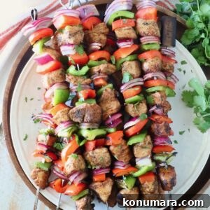 grilled chicken fajita skewers stacked up on a plate with fresh cilantro on the side