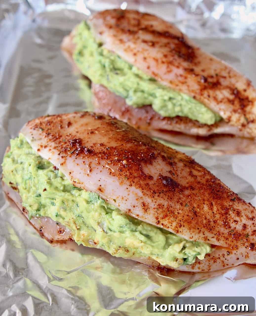 Uncooked guacamole stuffed seasoned chicken breasts on foil-lined baking sheet
