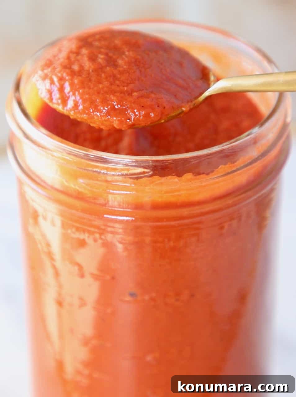 spoon of enchilada sauce lifted out of mason jar of sauce