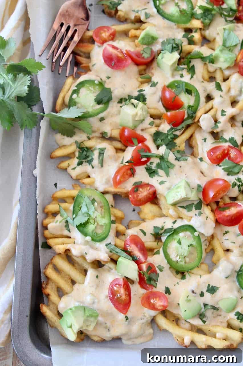 overhead image of waffle fries on baking sheet covered in cheese sauce