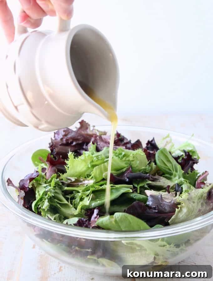 small pitcher pouring vinaigrette dressing on salad in a glass bowl