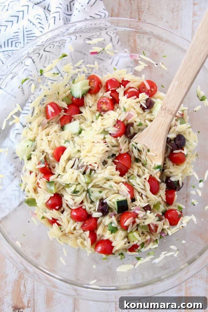 orzo salad in glass bowl with wooden spoon