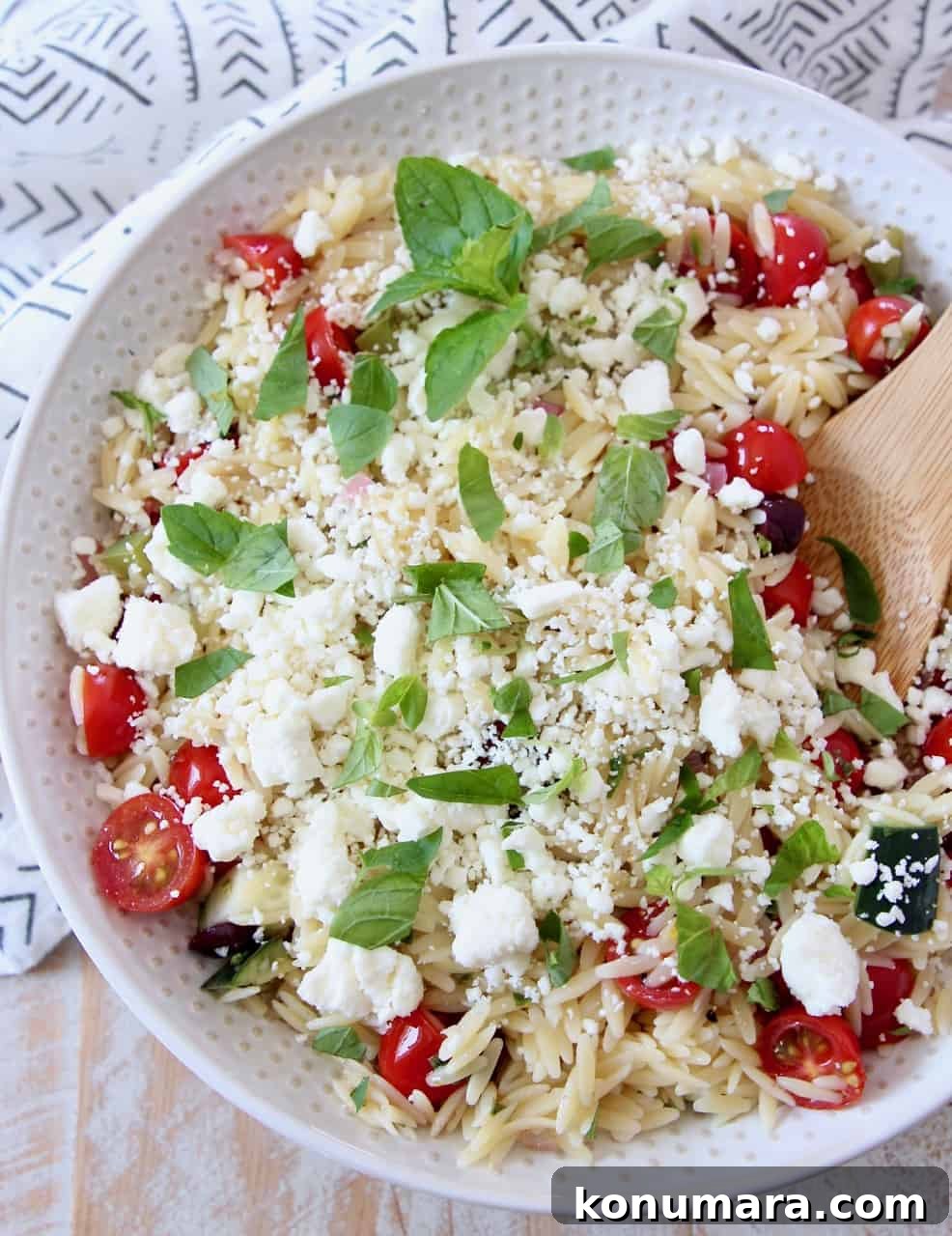 orzo salad with tomatoes and feta in bowl with wooden spoon