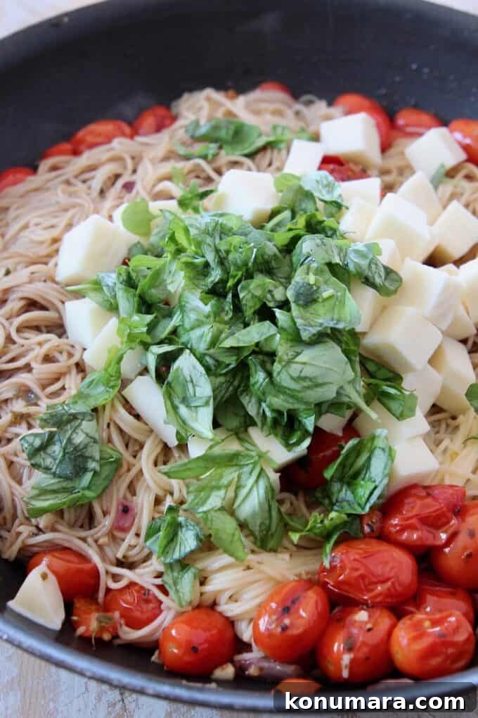 Caprese Pasta with Cherry Tomatoes, Mozzarella and Basil 11 cooked angel hair pasta in a skillet topped with fresh basil, cubes of mozzarella cheese and cherry tomatoes