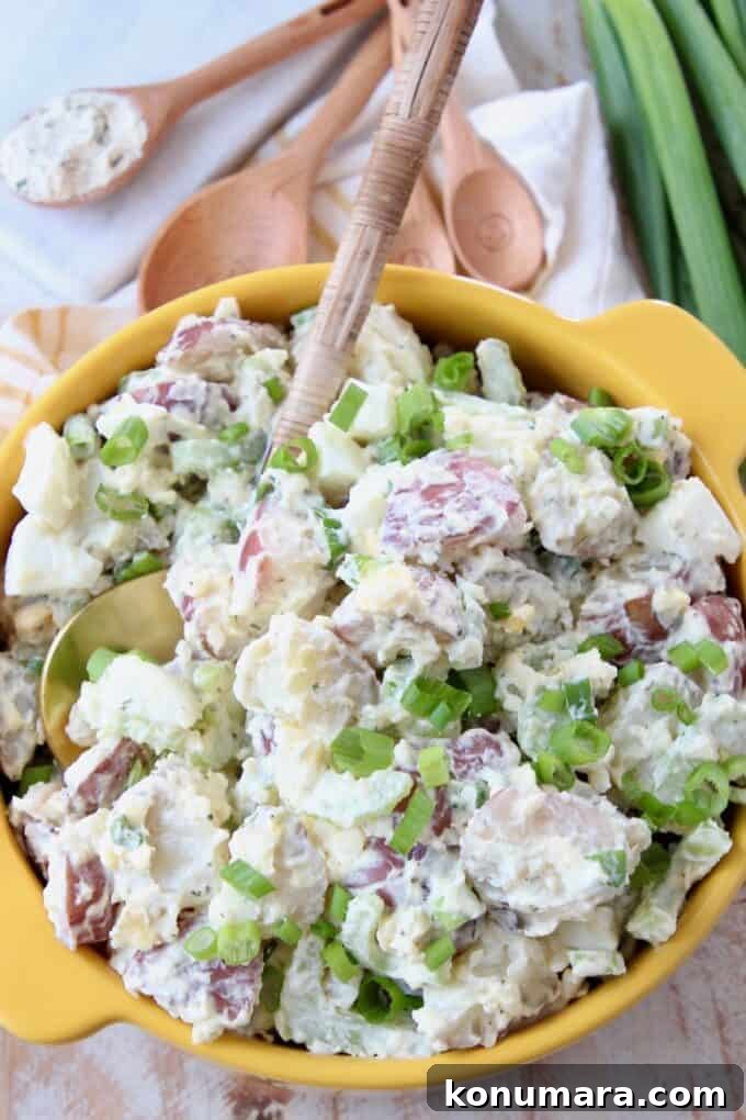 Instant Pot Cheddar Ranch Potato Salad Recipe 6 potato salad in yellow bowl with serving spoon and green onions on the side