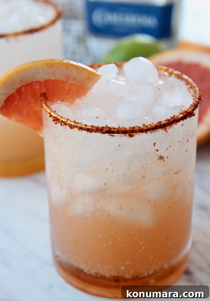 paloma in glass with ice and tajin rim on the glass with a grapefruit wedge