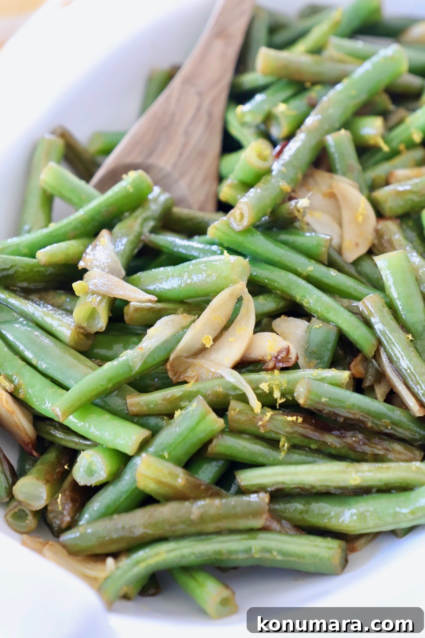 Sauteed Garlic Lemon Green Beans 2 cooked green beans in white serving bowl with wooden spoon