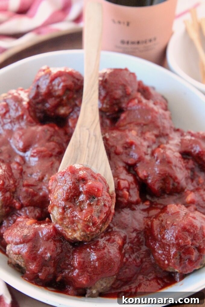 meatball covered in bbq sauce on spoon in bowl of meatballs