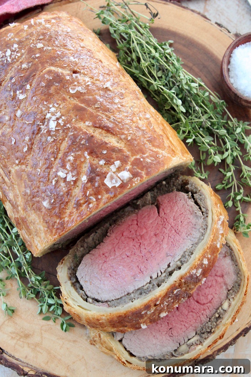 How to Make Classic Beef Wellington with Mushroom Duxelles 2 cooked, sliced beef wellington on wood serving tray with fresh herbs
