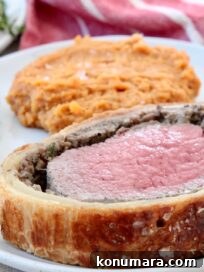 How to Make Classic Beef Wellington with Mushroom Duxelles 11 slice of beef wellington on plate with mashed sweet potatoes and fresh herbs