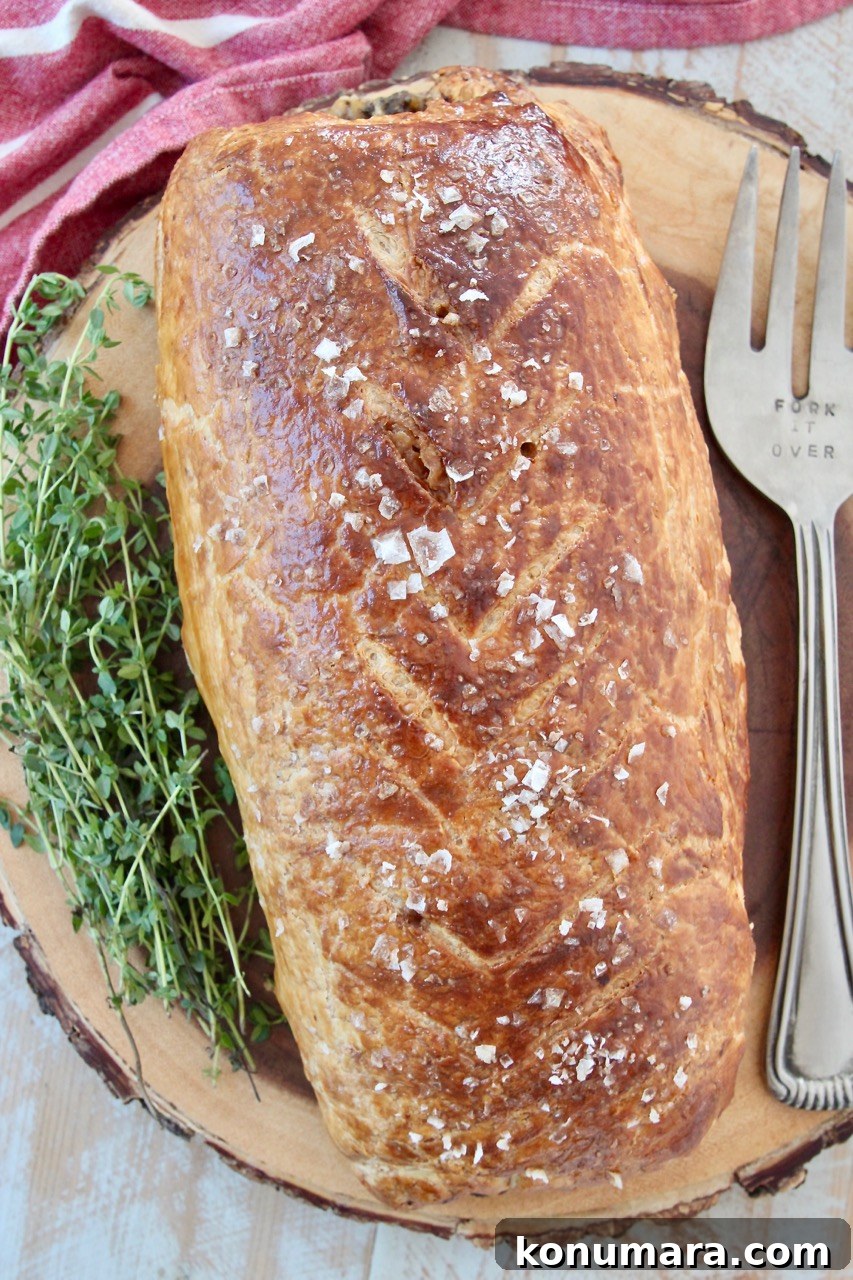 How to Make Classic Beef Wellington with Mushroom Duxelles 8 baked beef wellington on wood serving board with fresh herbs and serving fork
