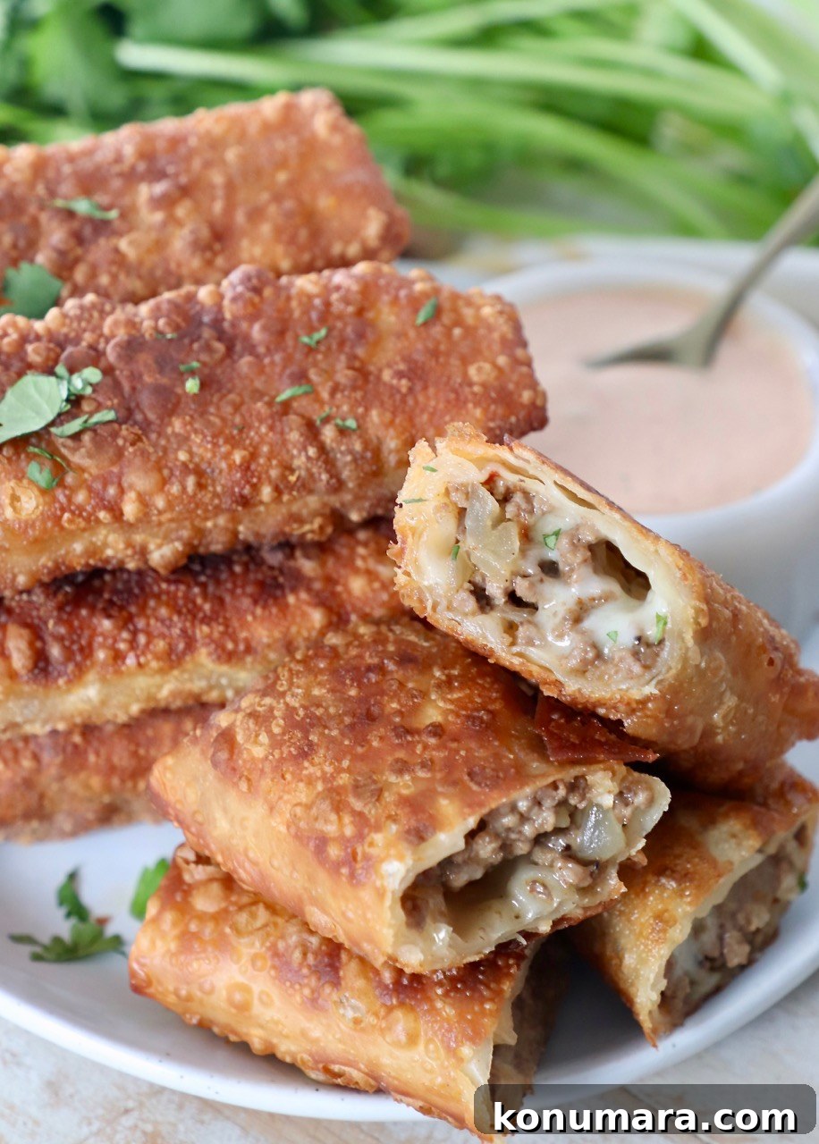 cheeseburger egg rolls stacked up on plate with side of thousand island dressing in white bowl