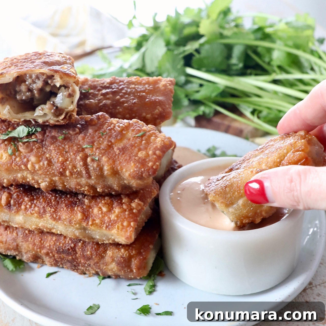 hand dipping cheeseburger egg roll into sauce in bowl