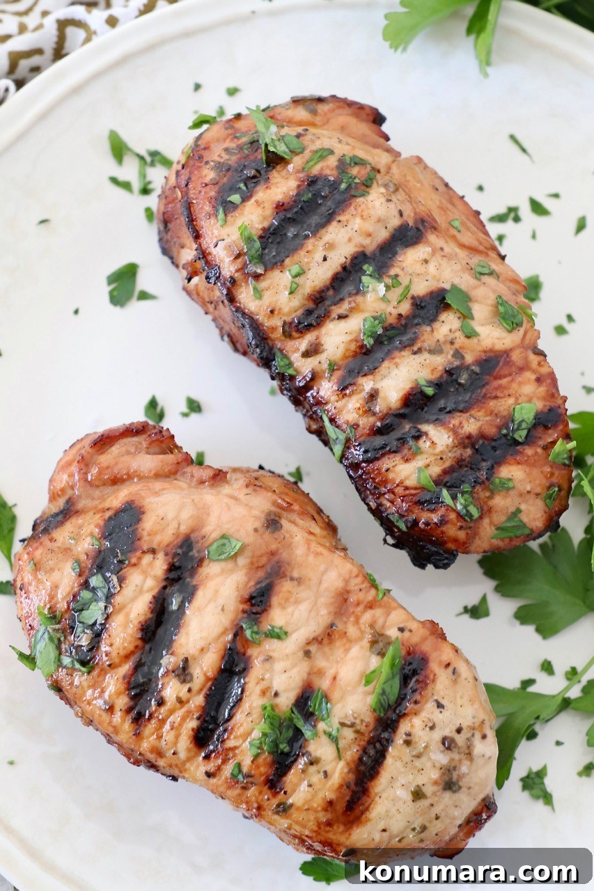 two grilled pork chops on plate topped with fresh chopped herbs