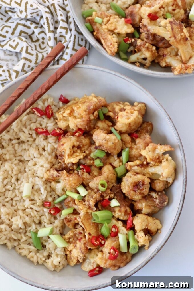 fried cauliflower in bowl with brown rice and chopsticks