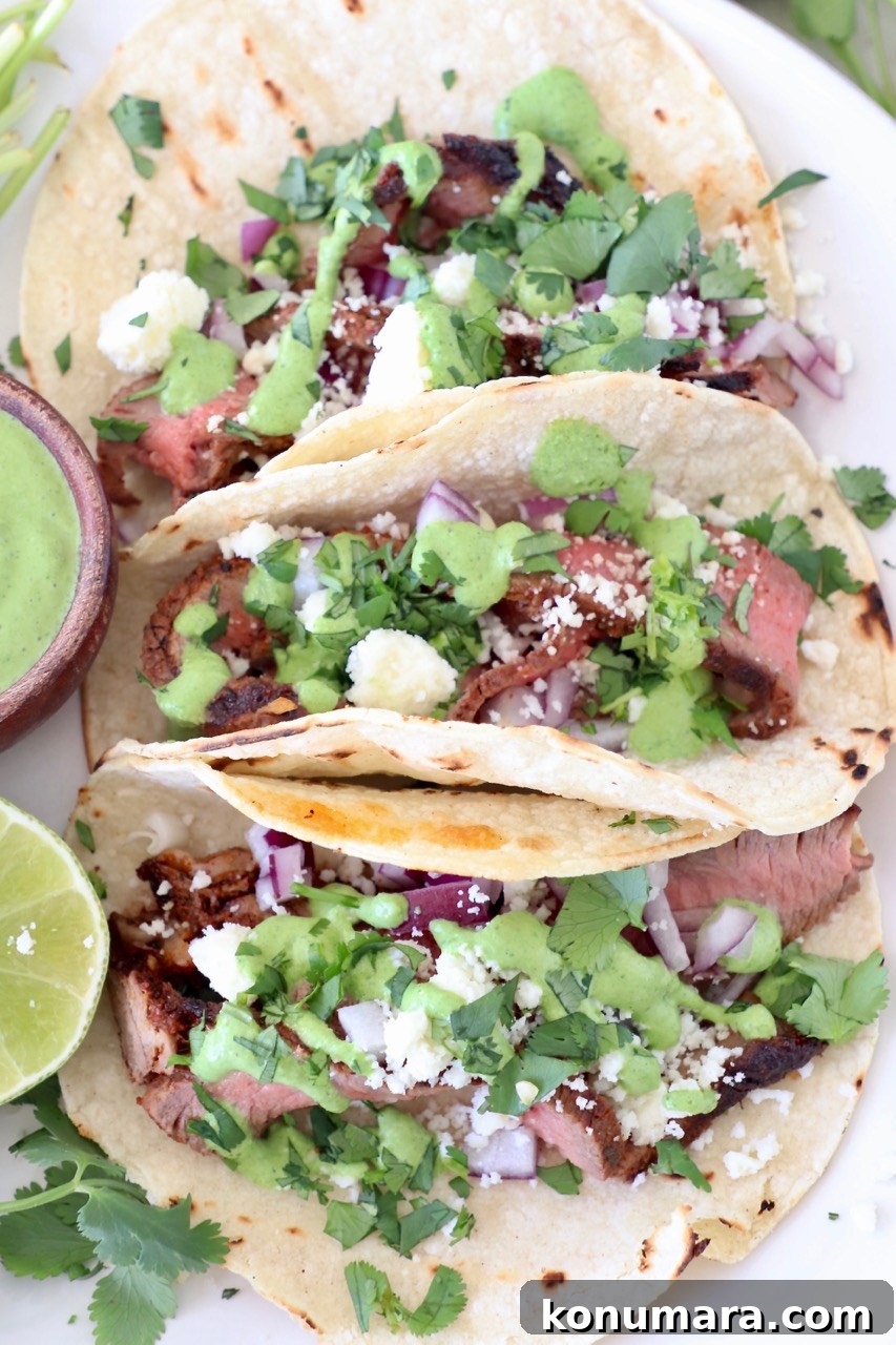 three steak tacos on plate topped with cilantro, sauce and cheese