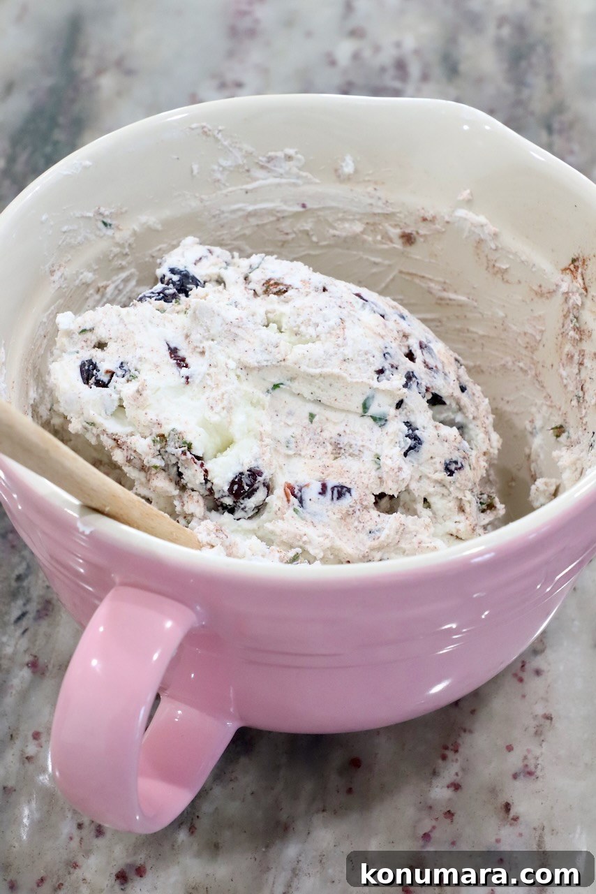 Goat cheese combined with dried cranberries and rosemary in a pink mixing bowl