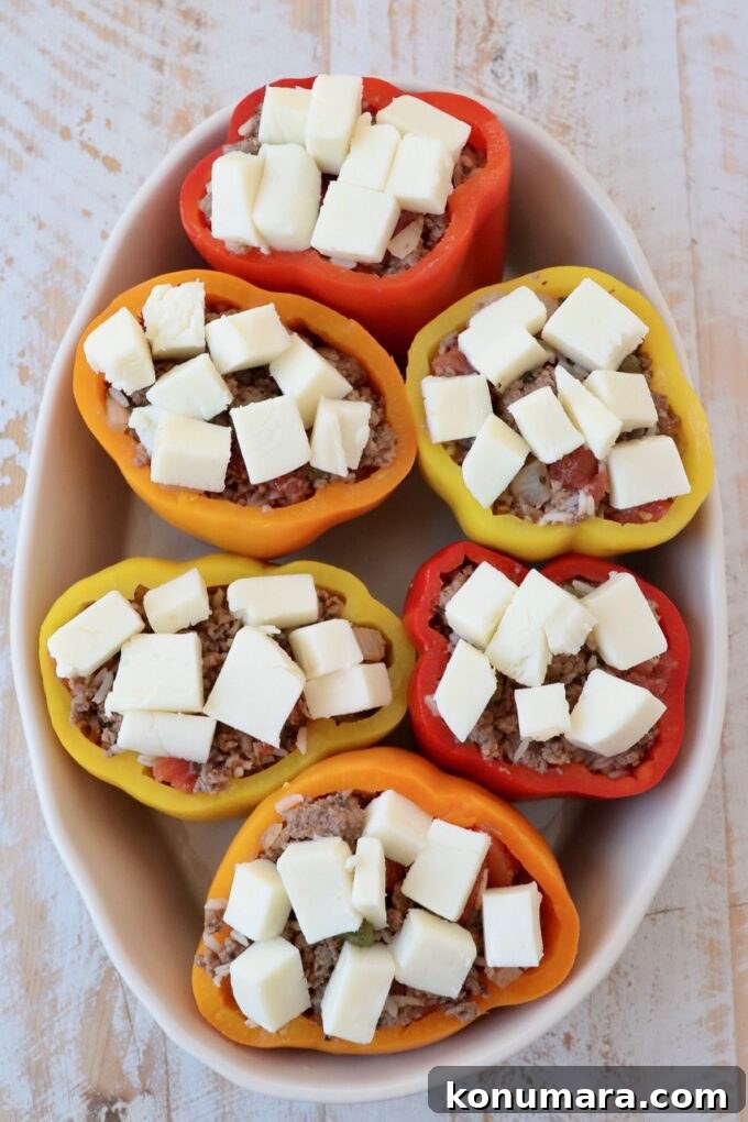 Stuffed bell peppers topped with cubes of cheese in oval casserole dish