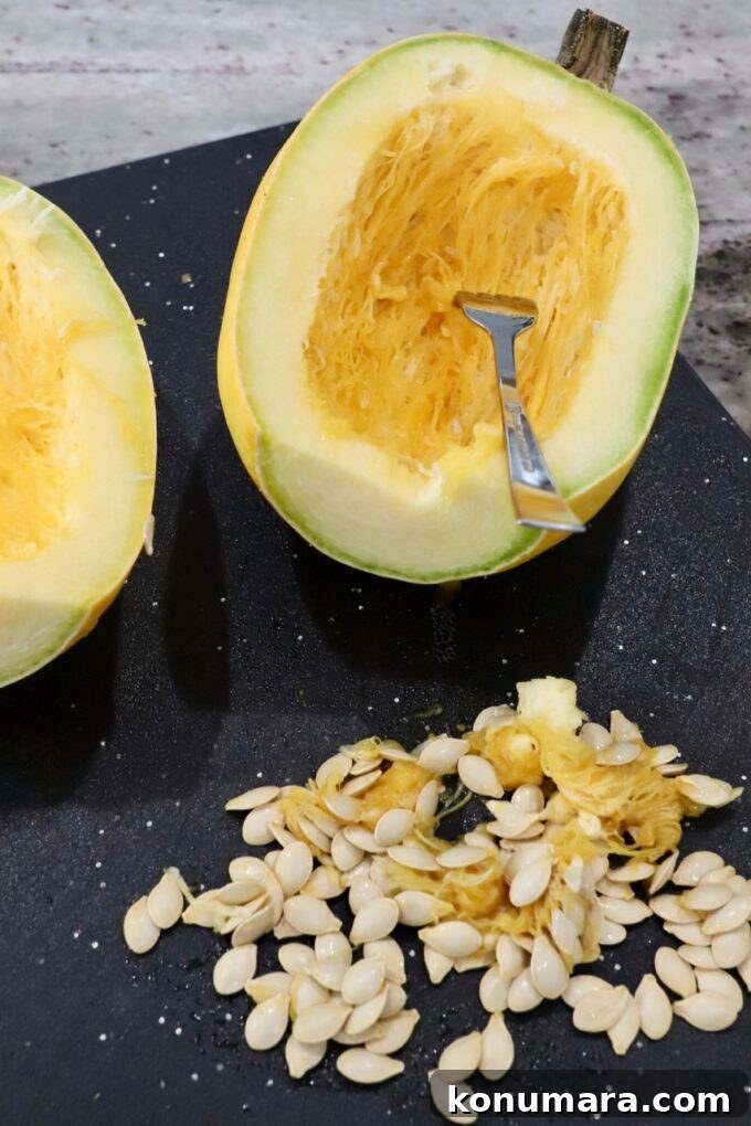 spaghetti squash cut in half on cutting board, with seeds removed on the side of the board