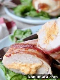 Juicy Bacon-Wrapped Stuffed Chicken Breasts Recipe 5 Bacon wrapped stuffed chicken breast cut in half on plate