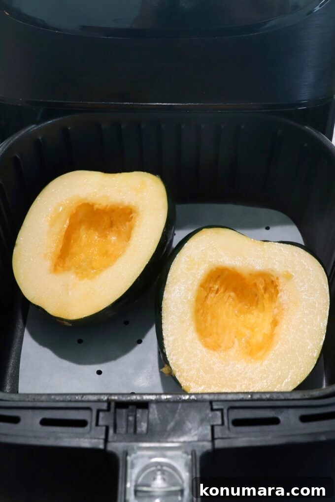 uncooked acorn squash cut in half in air fryer basket