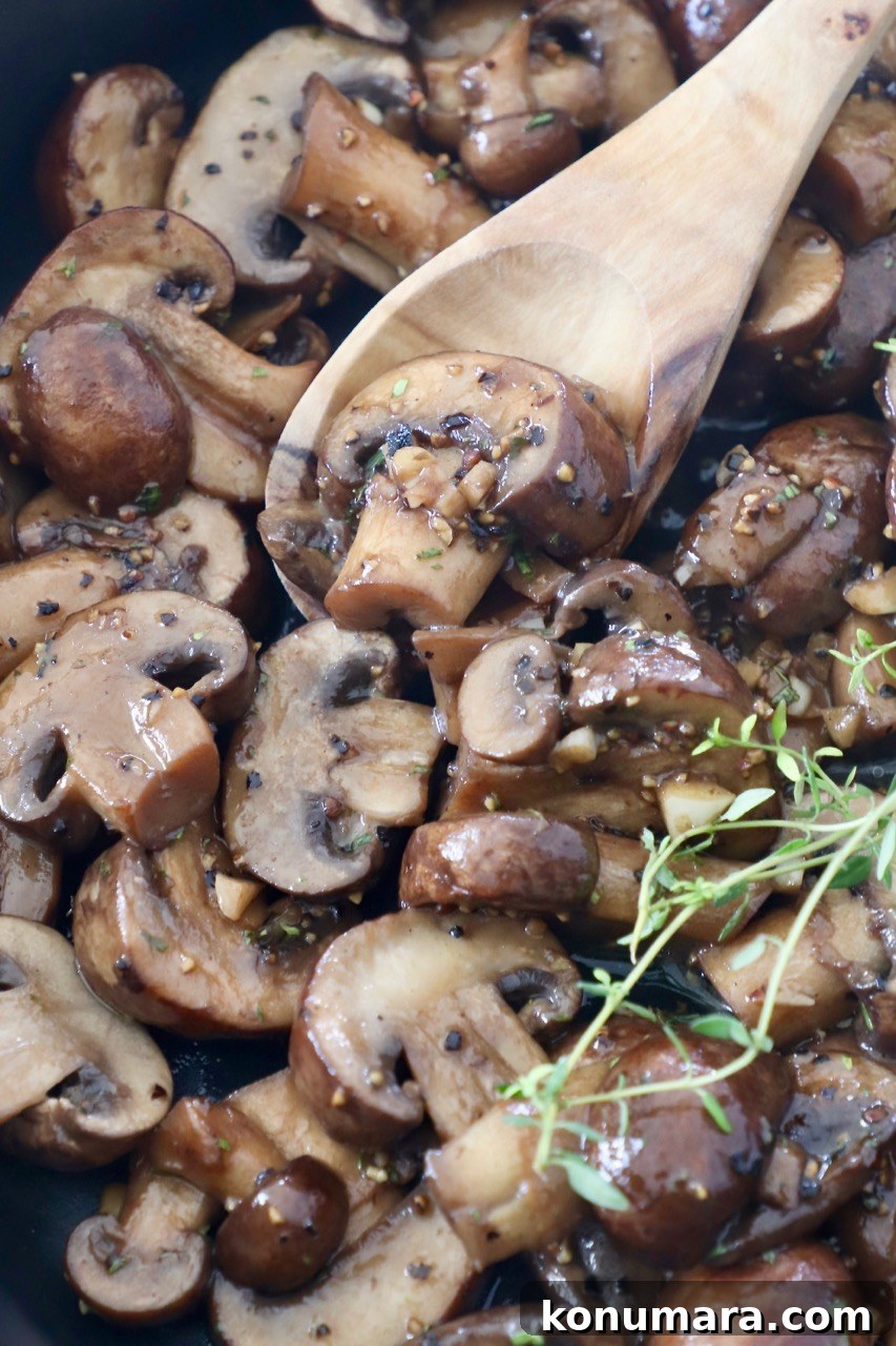 Garlic Butter Sauteed Mushrooms with Herbs 2 cooked sliced mushrooms in skillet with wooden spoon