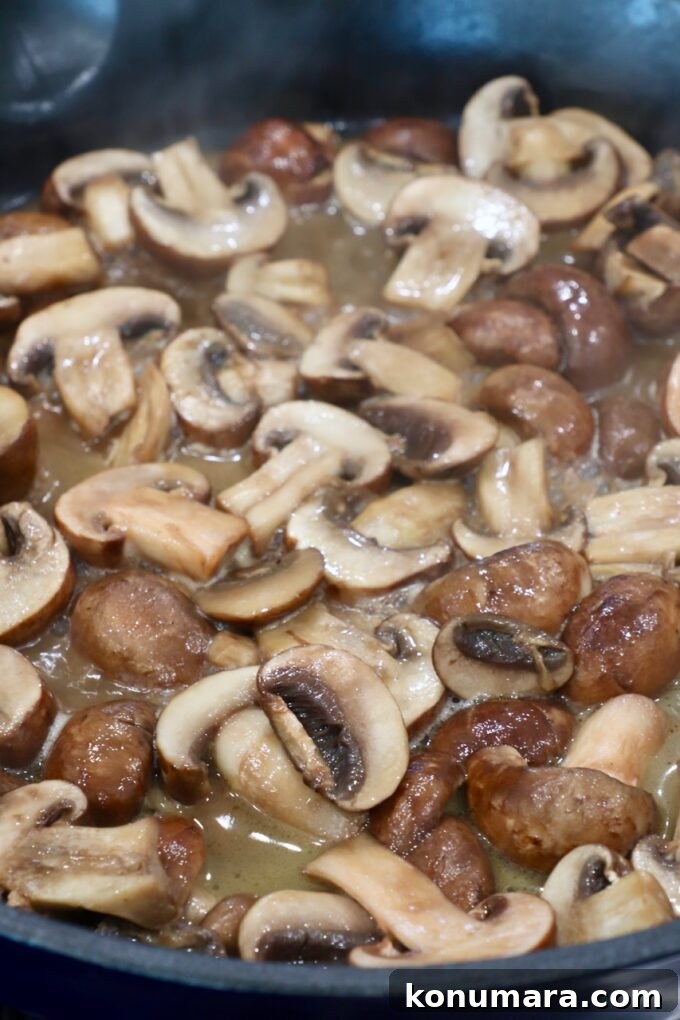 Garlic Butter Sauteed Mushrooms with Herbs 6 sliced mushrooms cooking in broth in skillet