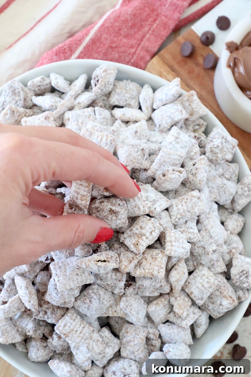 No-Bake Nutella Muddy Buddies Recipe 6 hand grabbing muddy buddies out of bowl