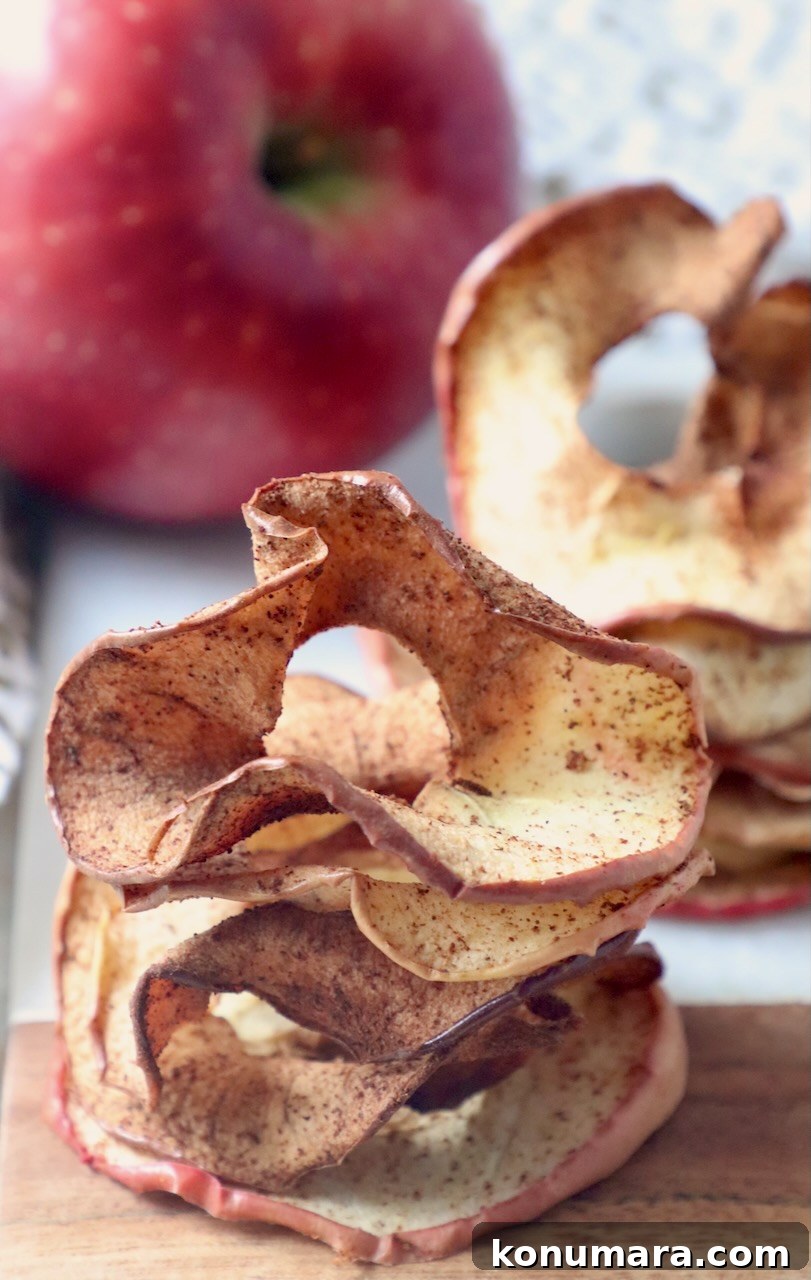 apple chips stacked up on cutting board with fresh whole apple