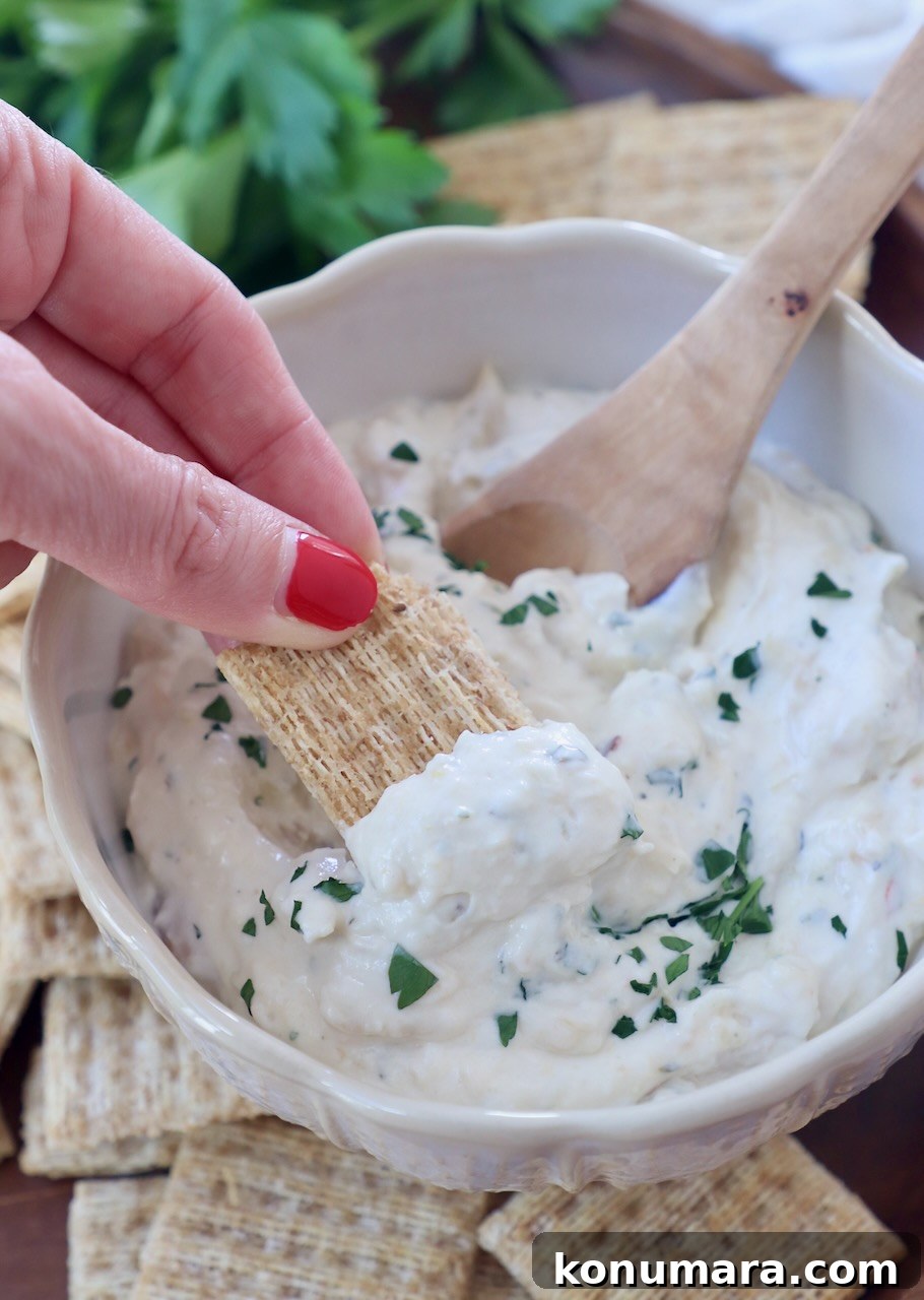 Creamy Roasted Garlic Dip Recipe 2 cracker dipped into garlic dip in bowl with wooden spoon