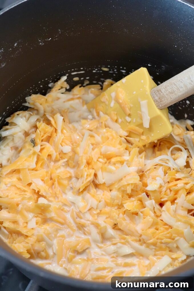 Homemade Nacho Cheese Sauce for Dips and Tacos 6 shredded cheese in pan with spatula