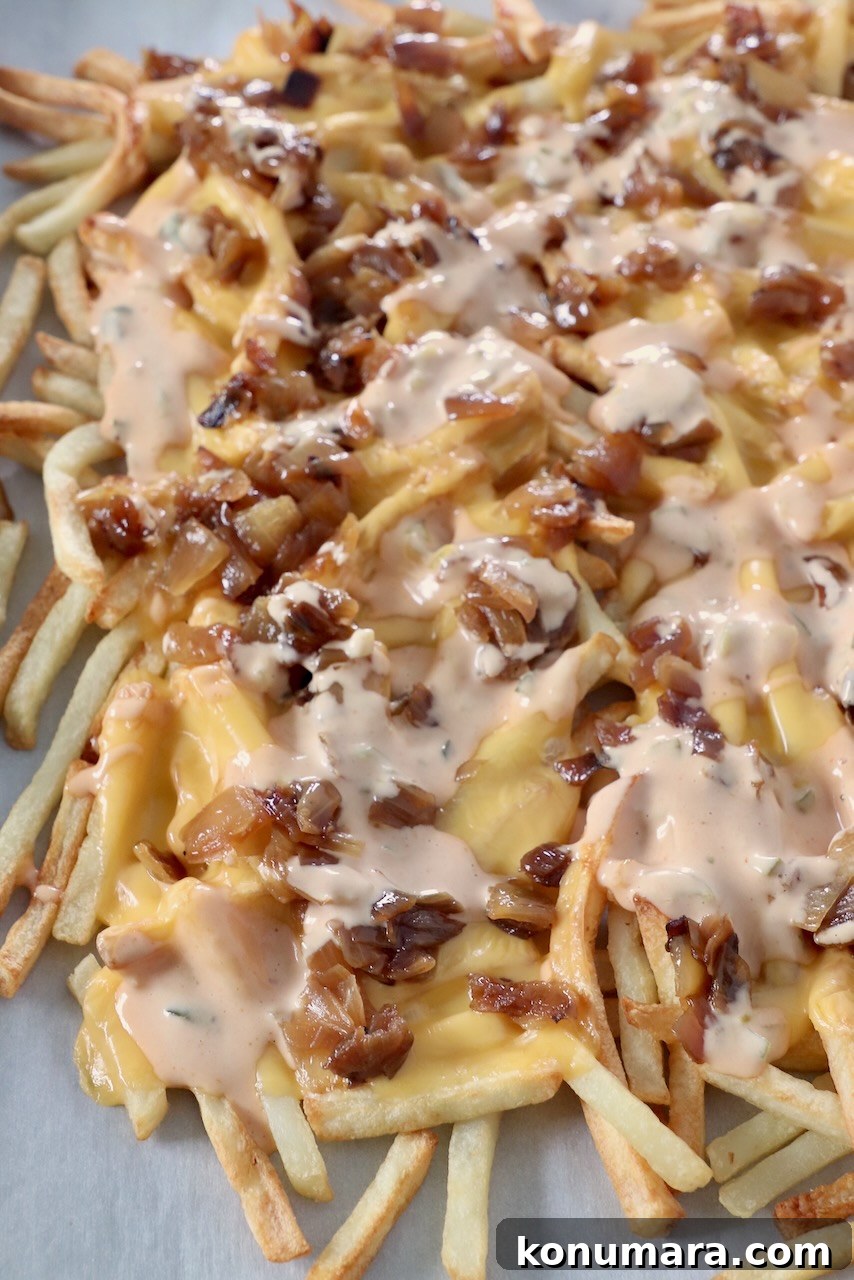 cooked french fries on baking sheet covered with cheese, caramelized onions and burger sauce