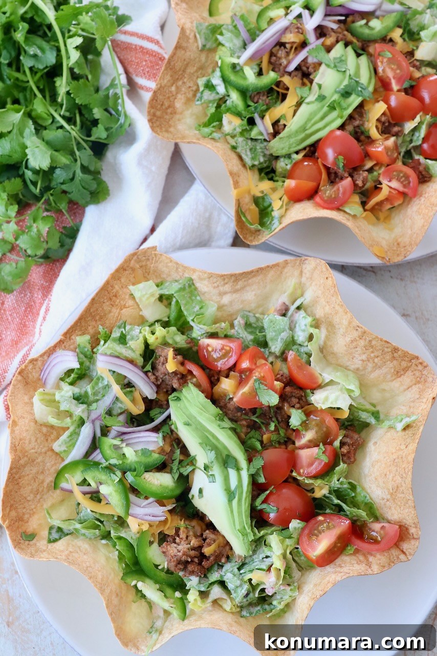 taco salad in tortilla shell bowl topped with sliced avocado on white plate