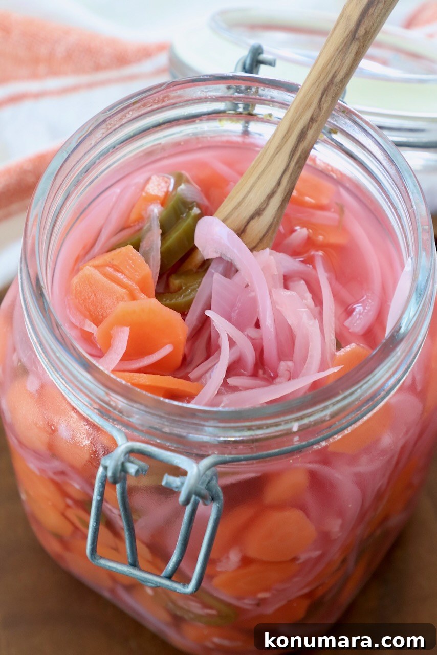 pickled sliced onions, carrots and jalapenos in large glass jar with wooden fork