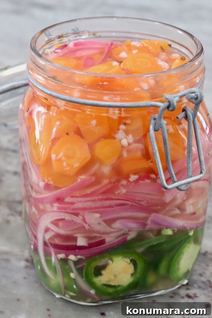 sliced carrots, onions and jalapenos in large glass jar covered in pickling liquid