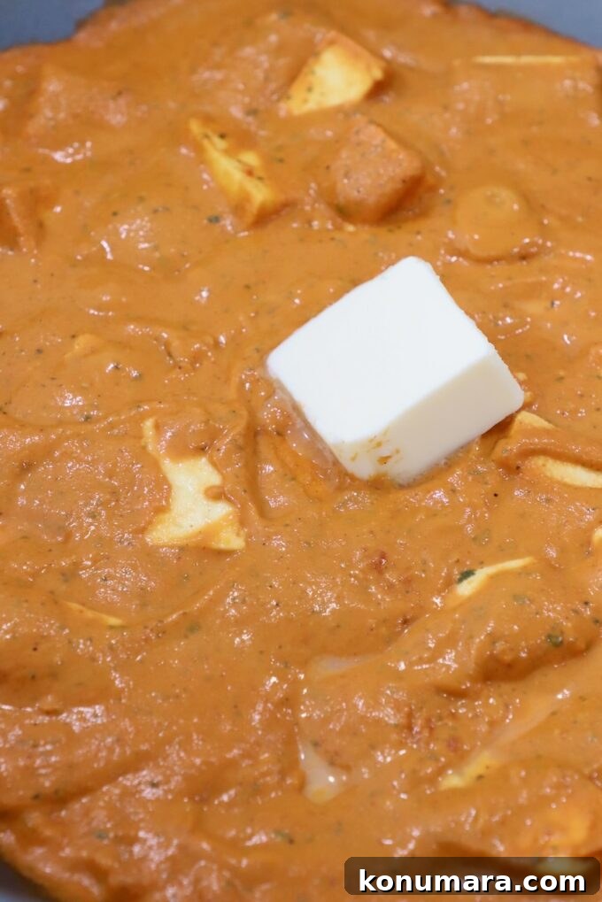 Paneer Makhani: Creamy Indian Butter Paneer Recipe 9 paneer in curry sauce in large pan topped with a cube of butter