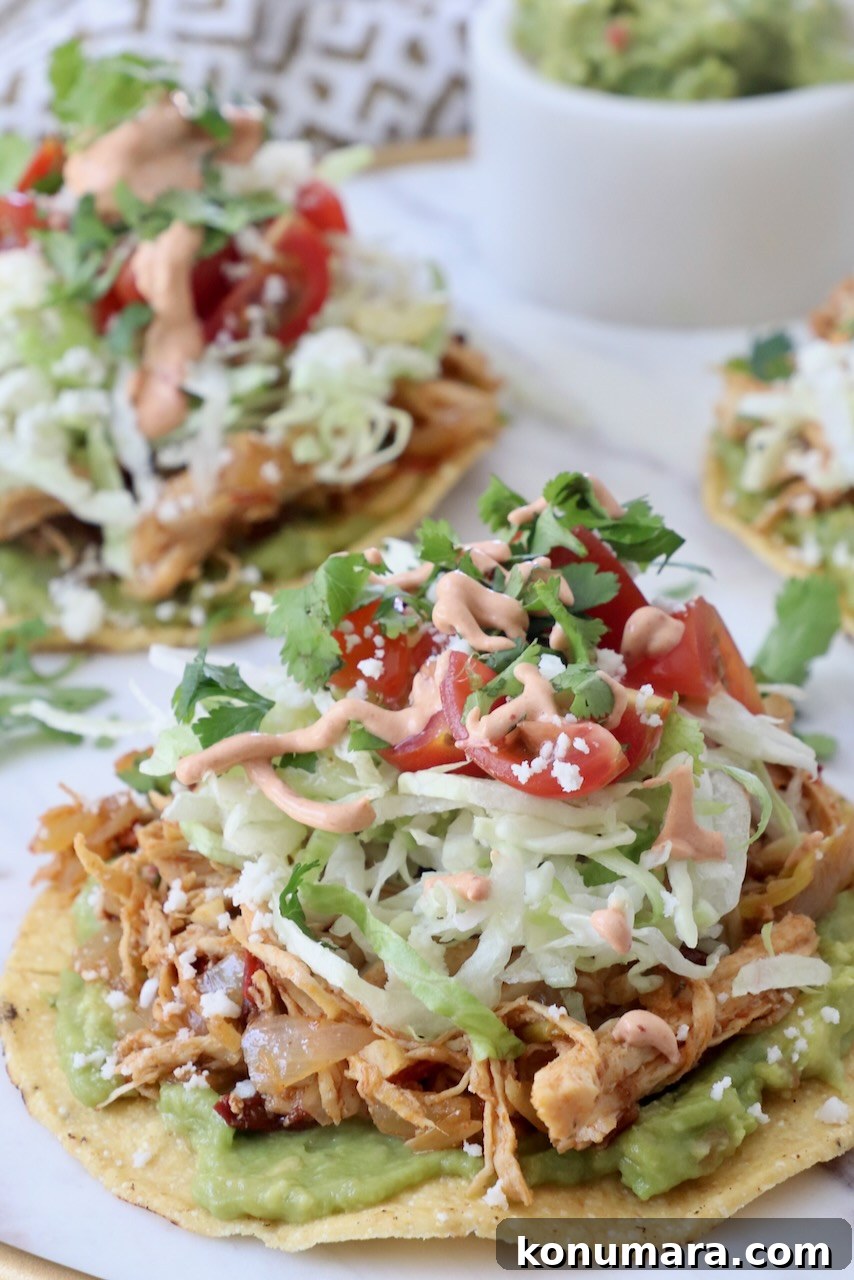 chicken tostada on plate topped with lettuce, tomato and creamy chipotle sauce