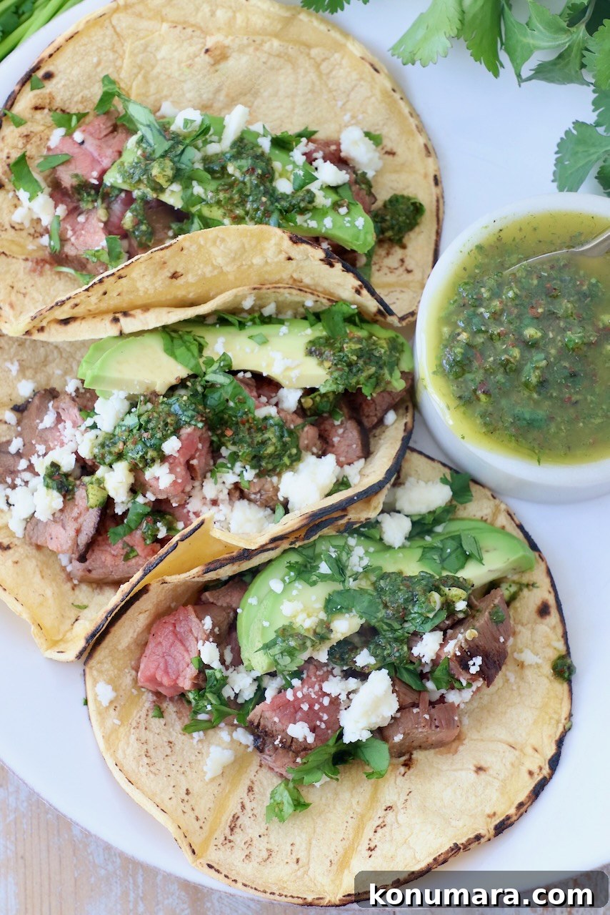 three tacos on plate filled with grilled steak, avocado and chimichurri sauce
