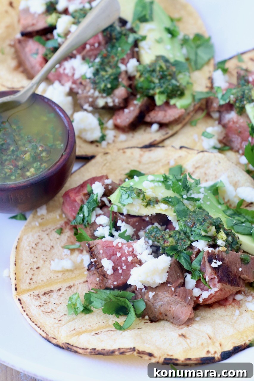 grilled steak in tortillas on plate topped with cotija cheese, avocado and chimichurri sauce