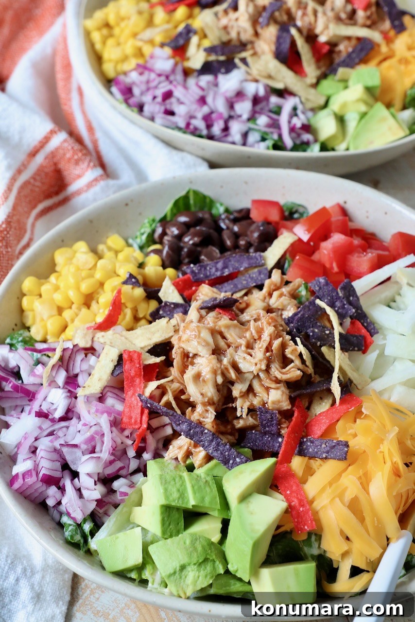 bbq chicken salad in bowl with diced onion, avocado, tomatoes, corn, black beans and cheddar cheese
