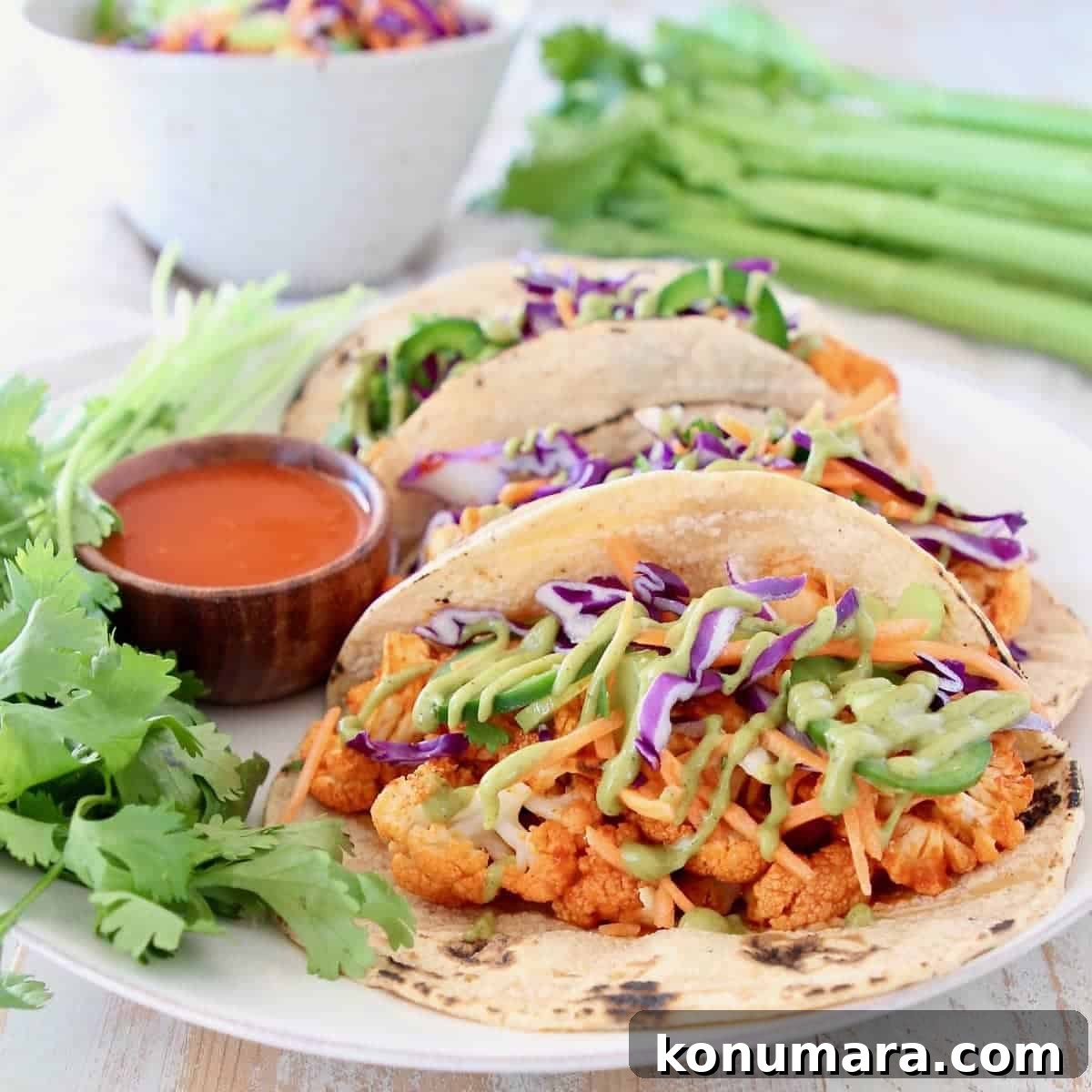 Buffalo cauliflower tacos on corn tortillas with jalapeno carrot slaw and fresh cilantro on plate with small bowl of buffalo sauce
