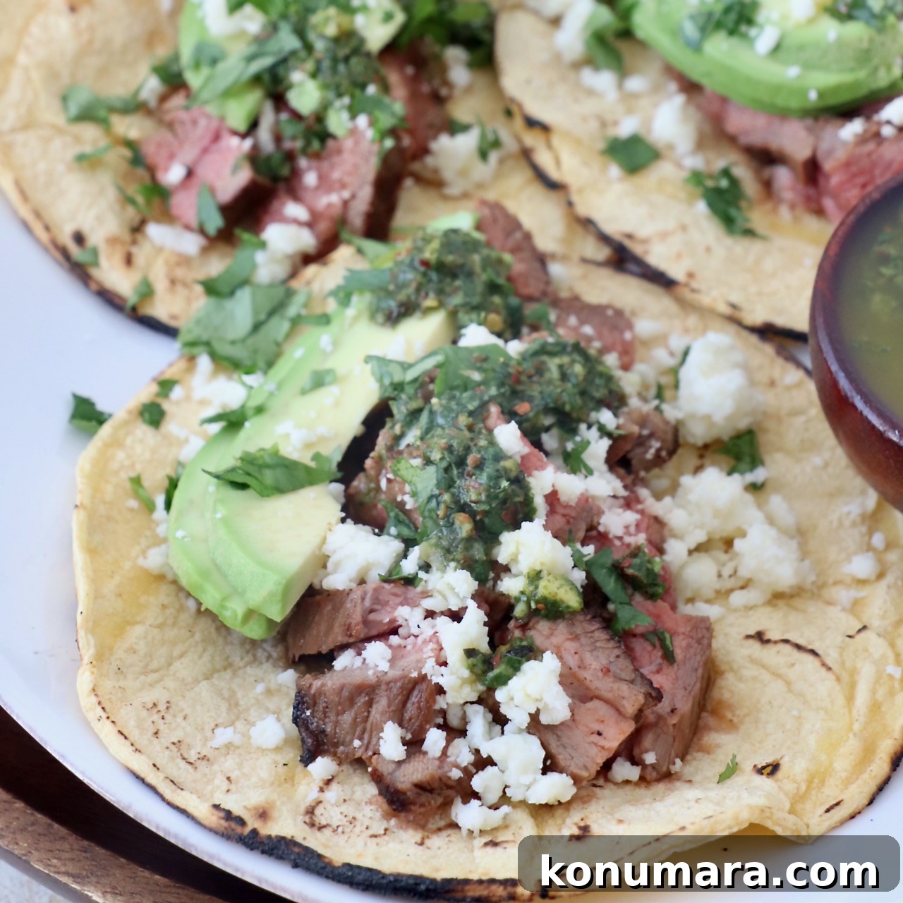 grilled diced steak in tacos with avocado and chimichurri sauce on white plate