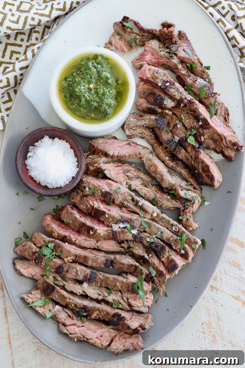 sliced grilled skirt steak on plate with small bowls of chimichurri sauce and flaky sea salt
