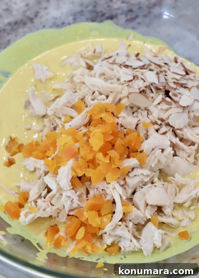 cooked, shredded chicken in large glass bowl with creamy curry sauce and diced dried apricots