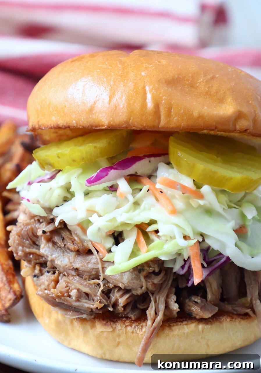 Tender and Juicy Instant Pot Pulled Pork Recipe 6 pulled pork sandwich topped with coleslaw and pickles on plate