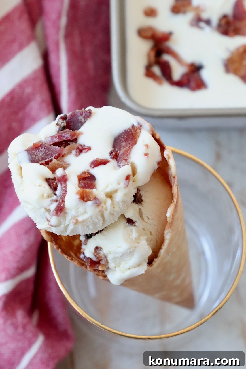 scoops of maple bacon ice cream in a waffle cone, held up in a drink glass
