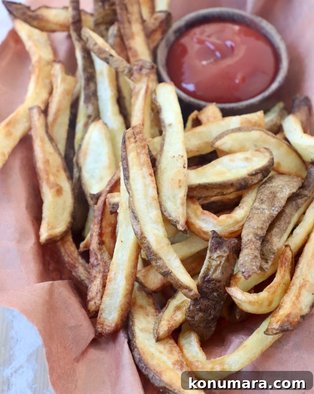cooked french fries in basket with small bowl of ketchup